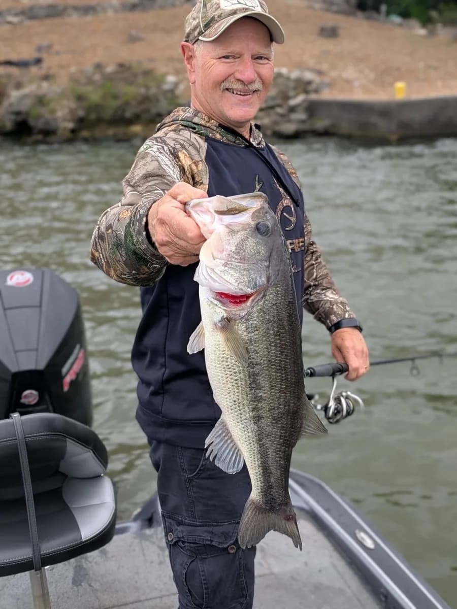 An angler in camo with a largemouth bass beside the boat
