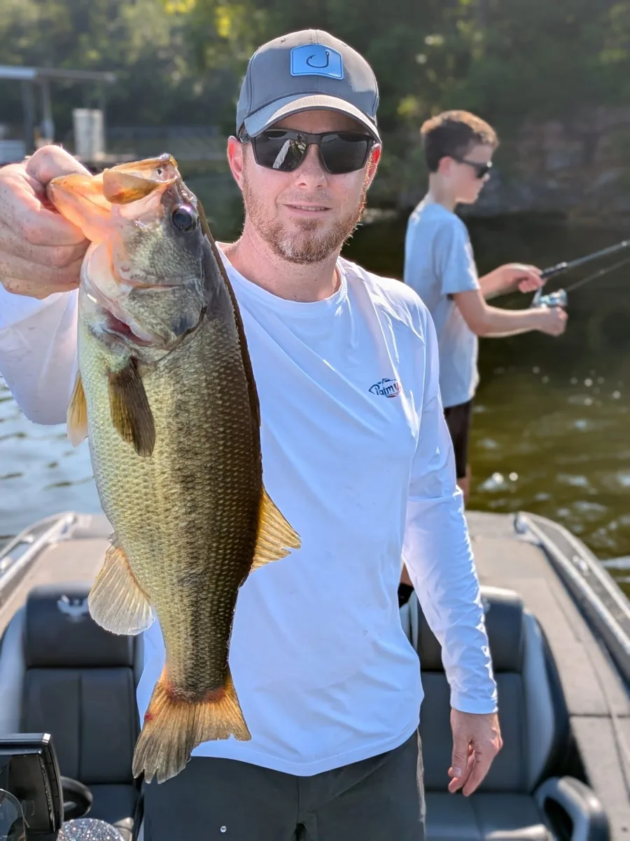 An angler with a largemouth bass while his partner keeps casting