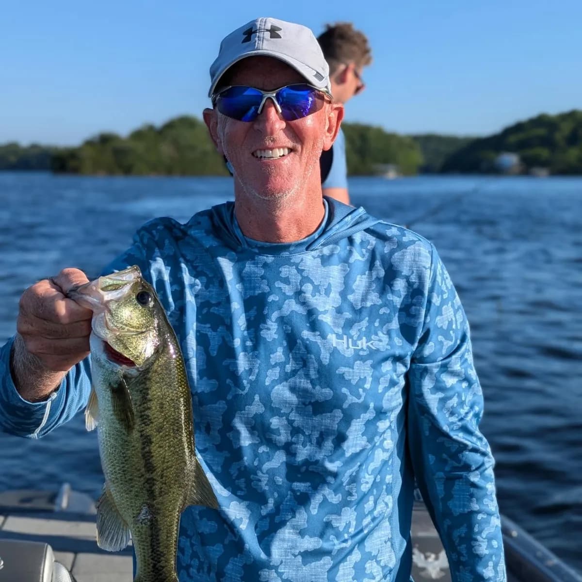 An angler in a sun shirt holding a spring largemouth bass
