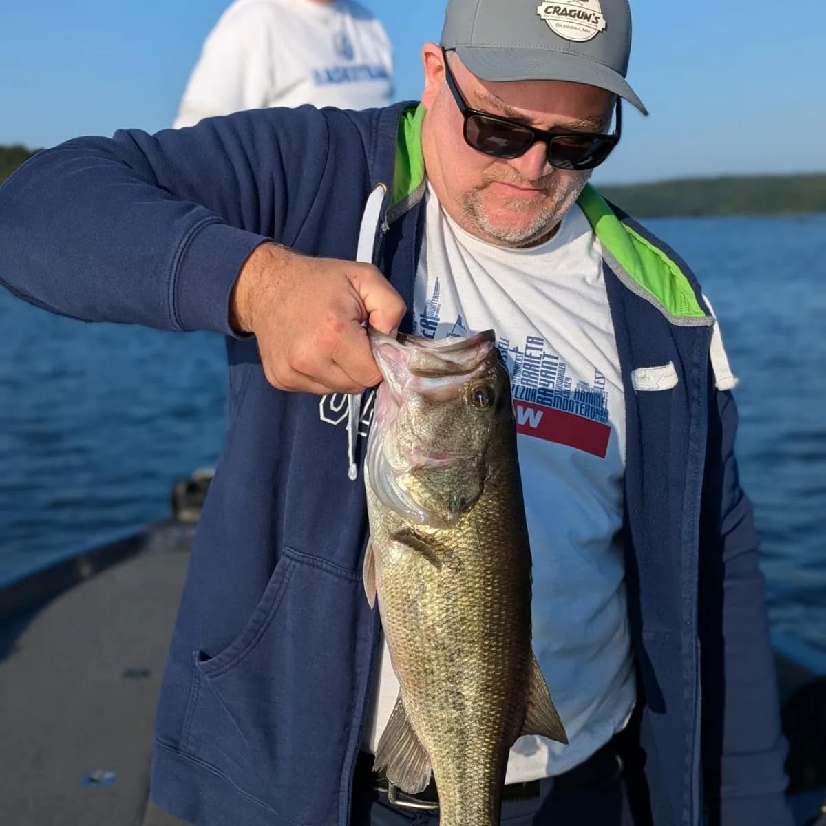 An angler in a jacket with a largemouth bass on a cool April morning