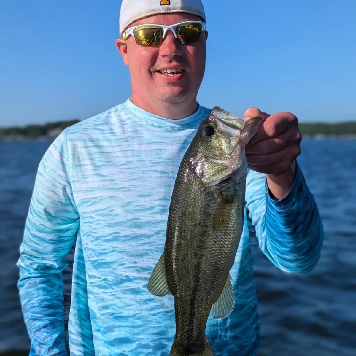 An angler in a light sun shirt with an April largemouth bass