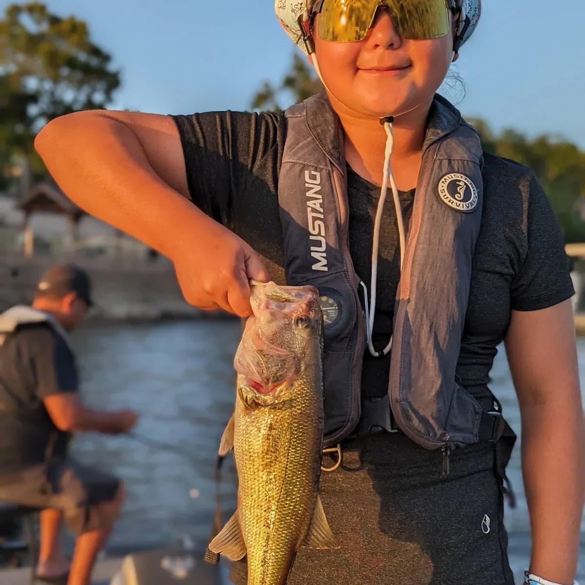 A young angler in an inflatable life vest holding a largemouth bass
