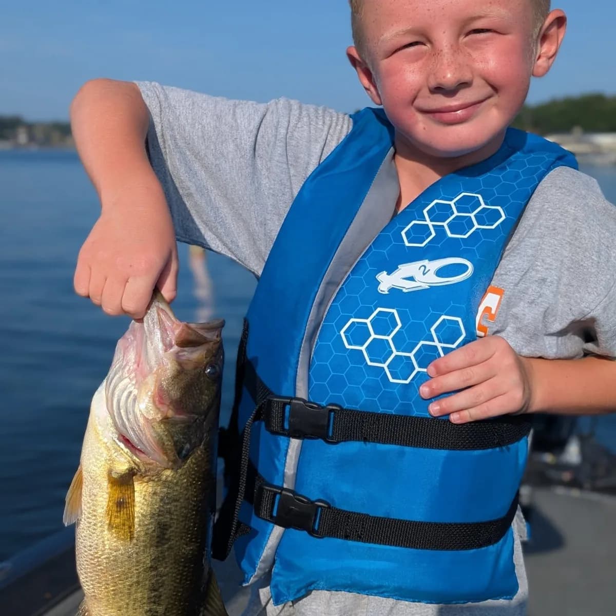 A young angler in a life jacket with an August largemouth bass