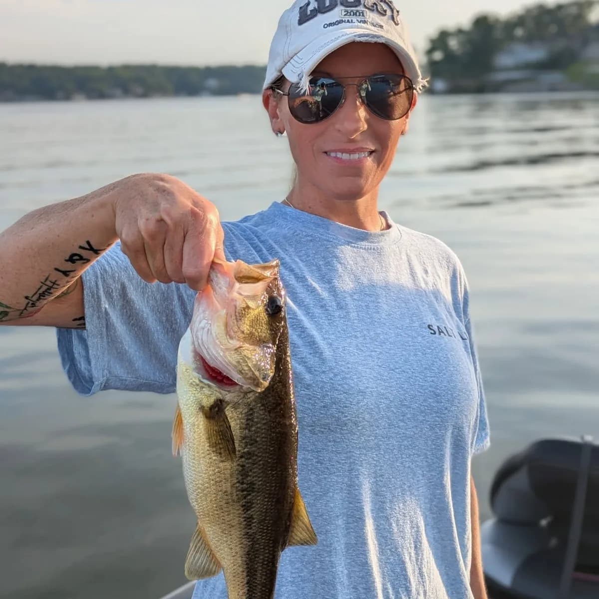 An angler holding a largemouth bass on a calm August morning