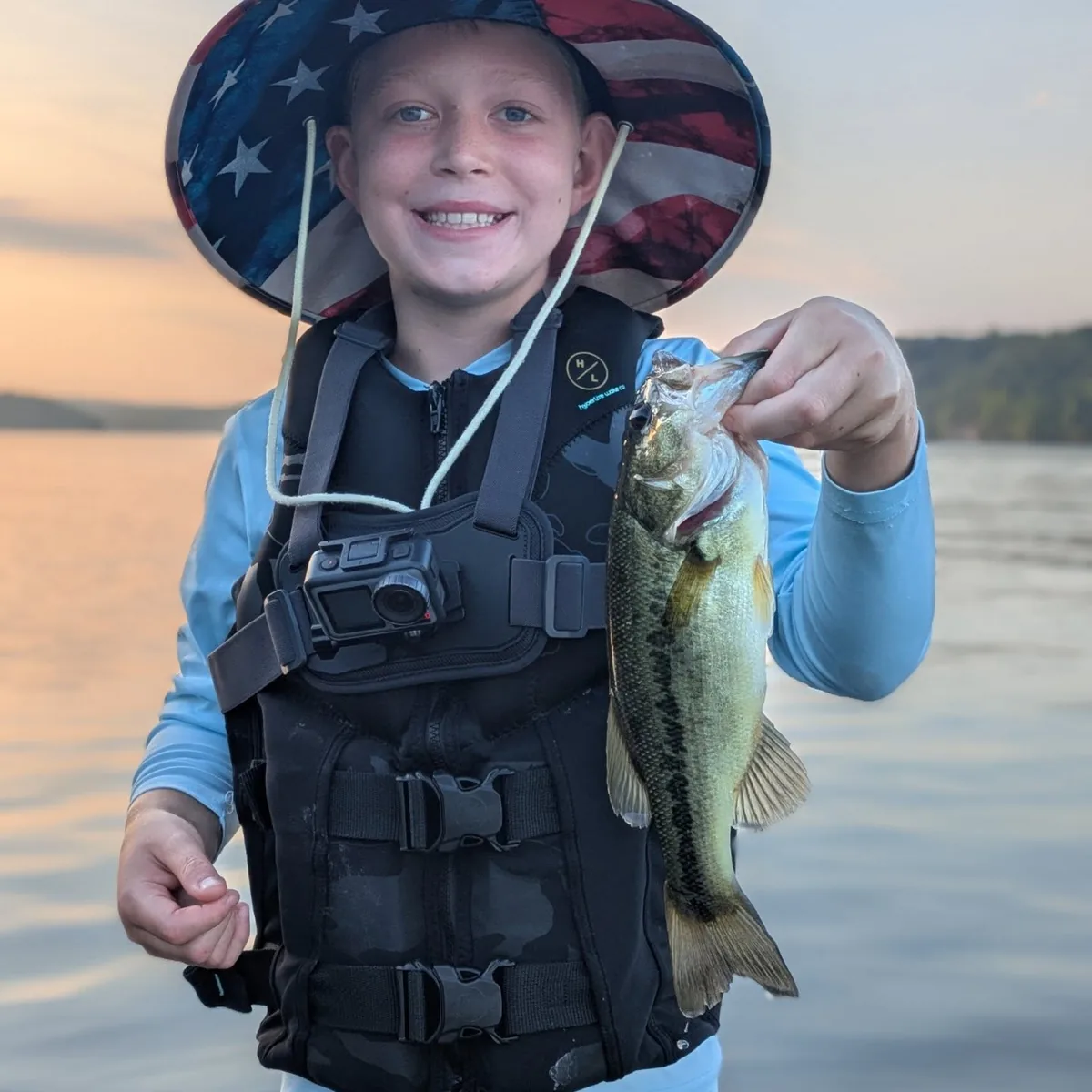 A young angler holding a largemouth bass at sunset