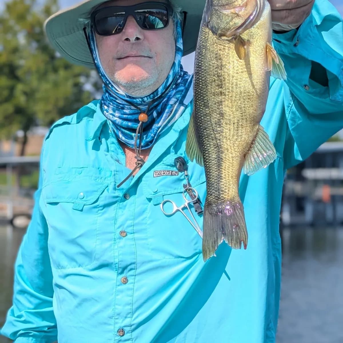 An angler in a sun mask holding a largemouth bass