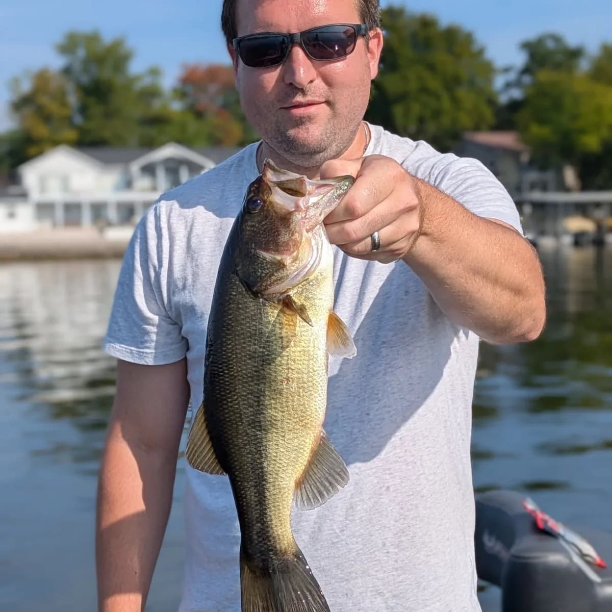 An angler with a largemouth bass in front of the shoreline