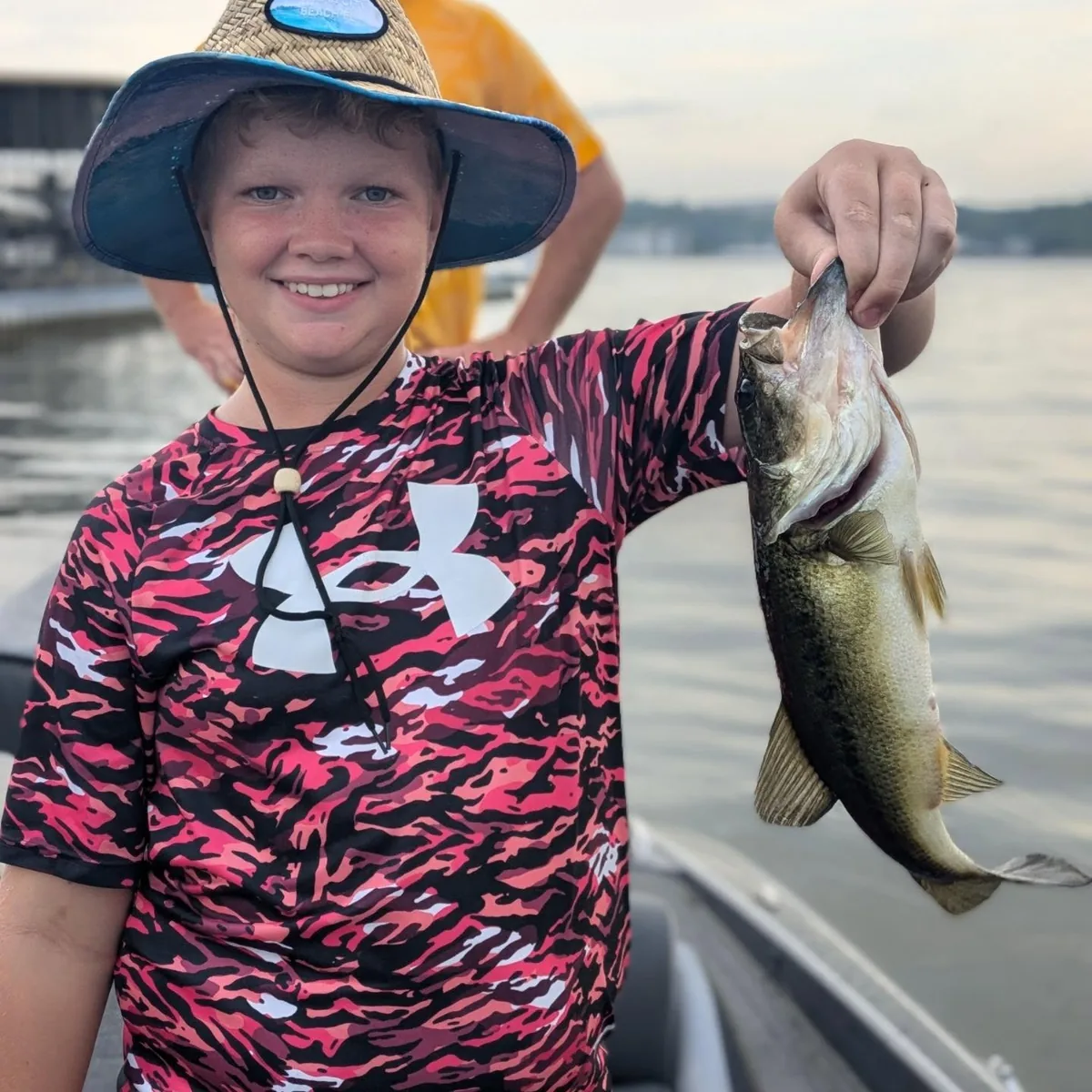 A young angler in a sun hat holding a largemouth bass