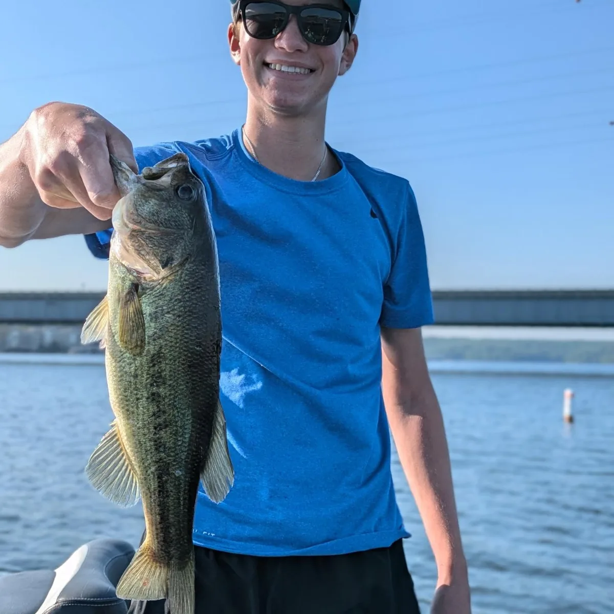 A teenage angler in a blue shirt with a largemouth bass
