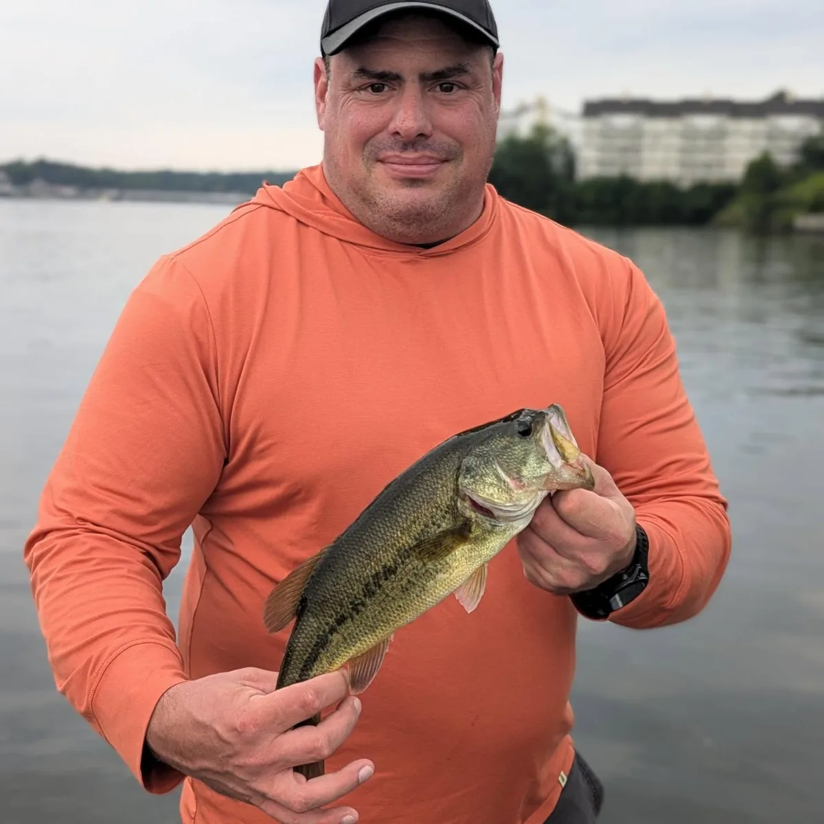 An angler in an orange sun shirt with a largemouth bass