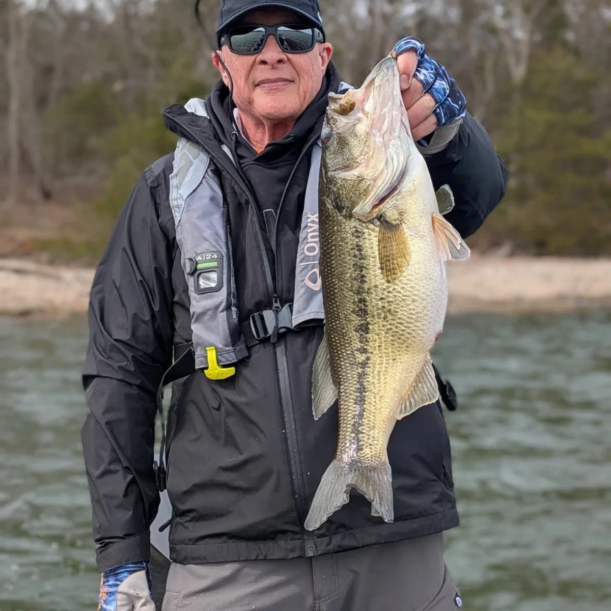An angler in a winter jacket and life vest with a pair of largemouth bass