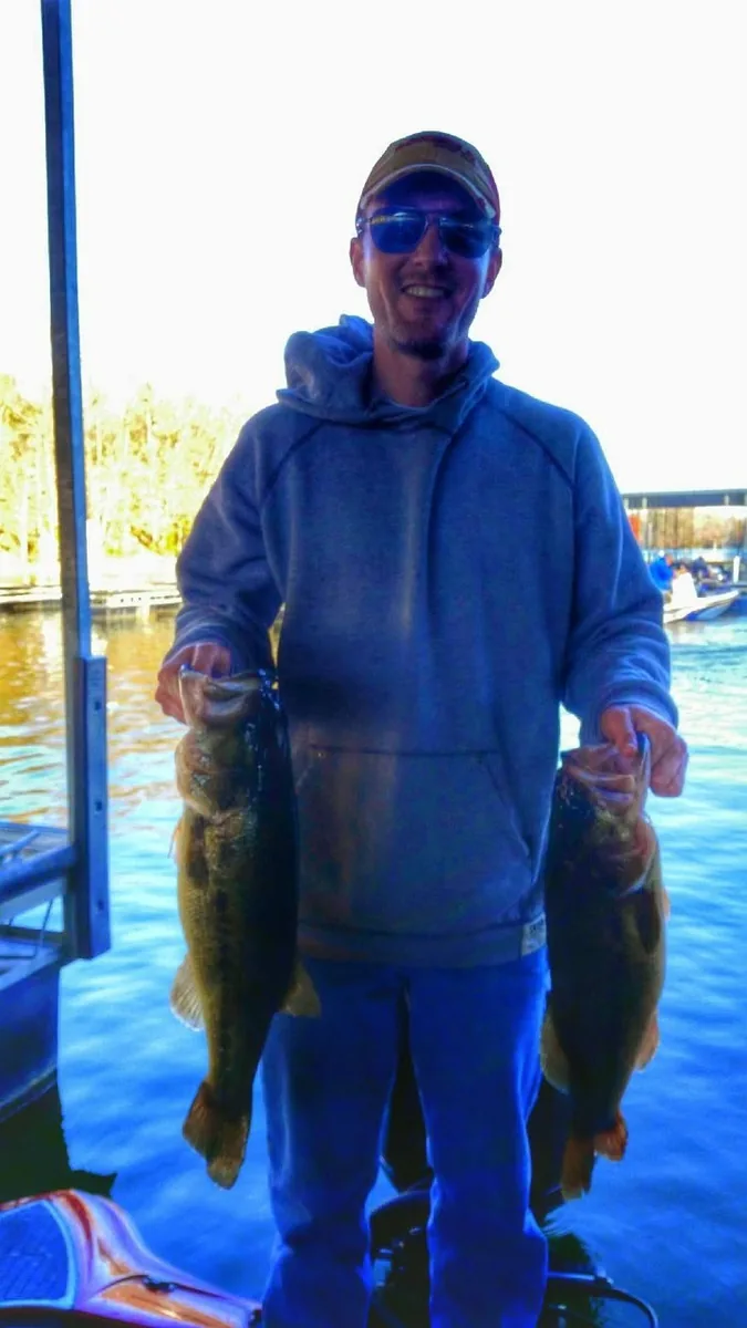 An angler in insulated coveralls with two bass caught under a dock
