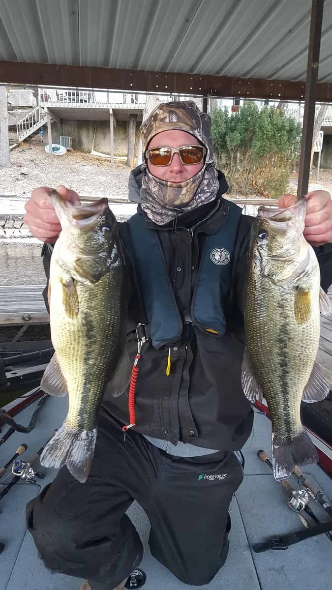 An angler in a face mask and life vest with two largemouth bass caught under a dock