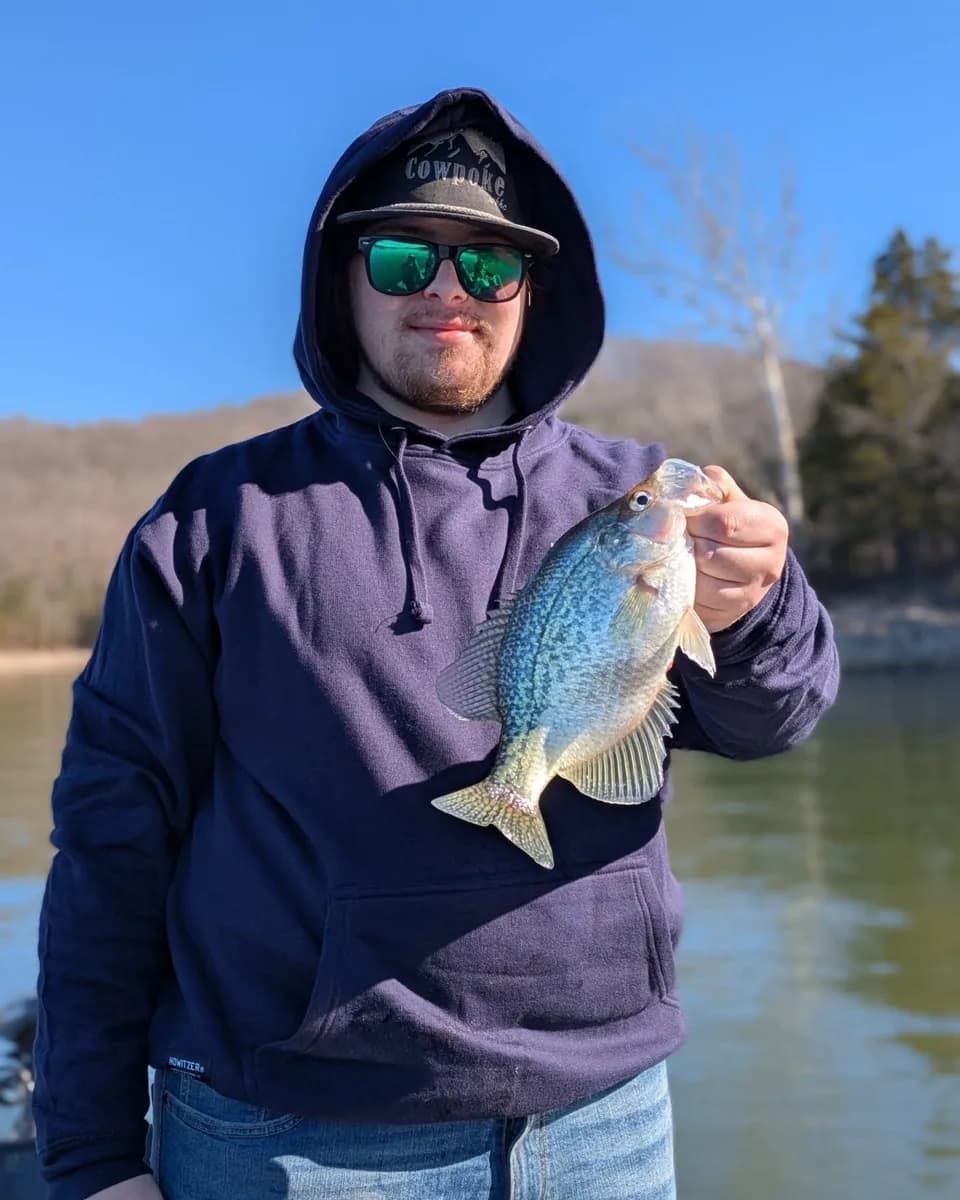 An angler in a hooded sweatshirt holding a crappie caught in January