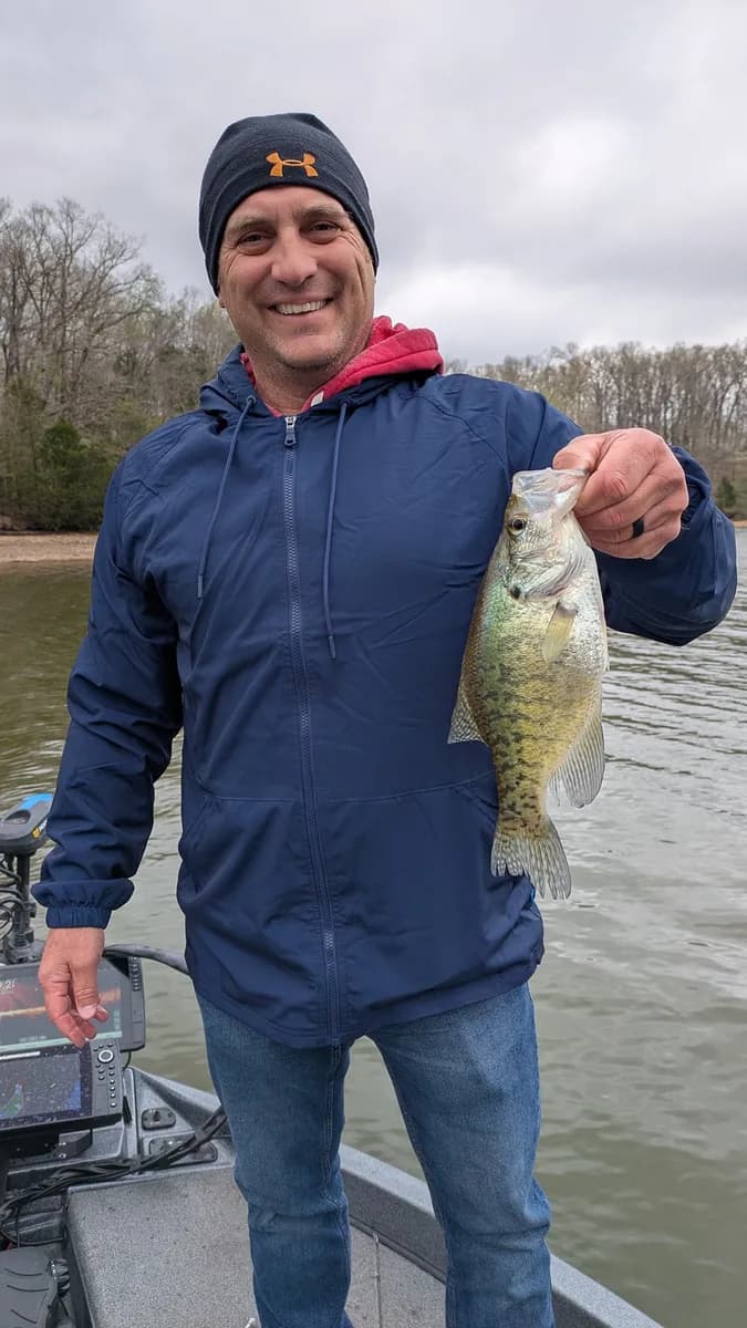 An angler in a beanie and winter jacket with a crappie caught in January