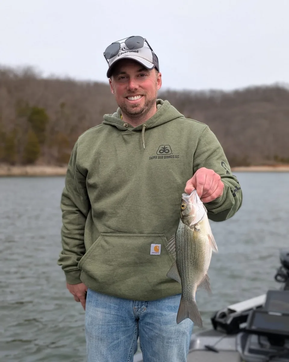An angler in a hoodie with a crappie caught beside the boat