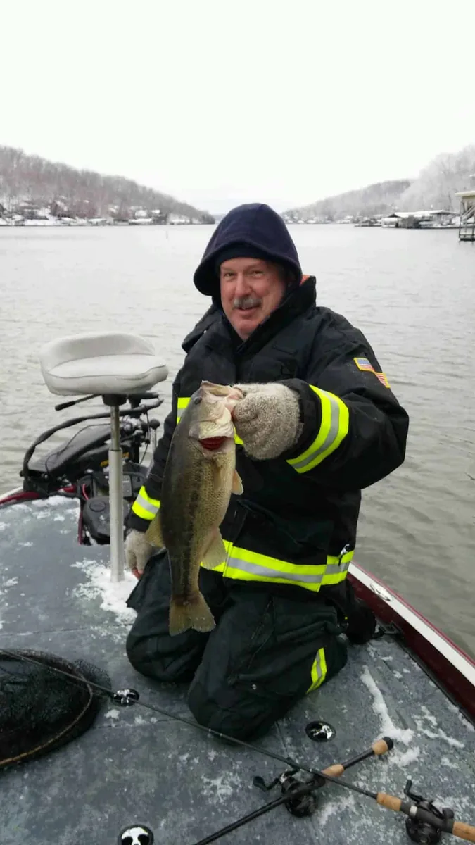 An angler with his hood up holding a largemouth bass from the deck in the cold