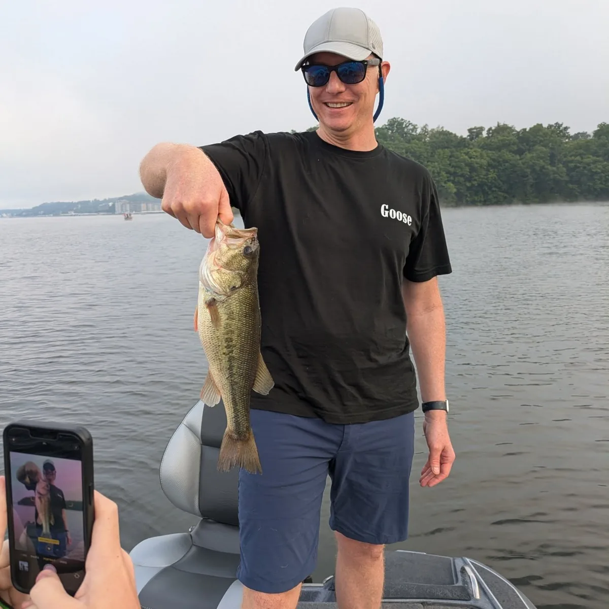 An angler holding a largemouth bass while the catch is filmed