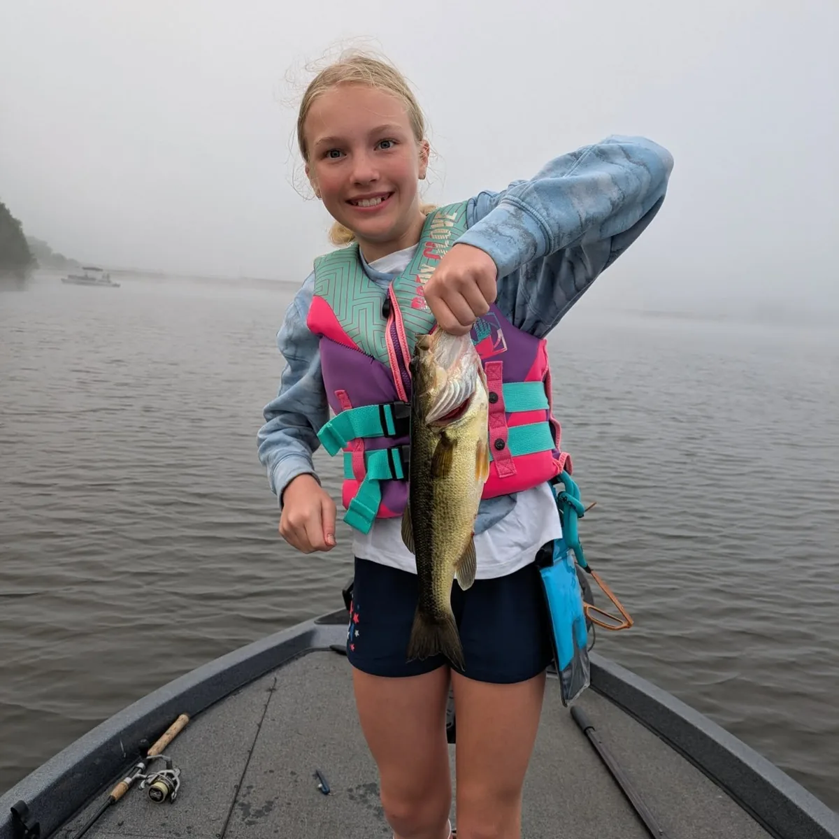 A young angler in a life jacket with a fish caught on a foggy July morning