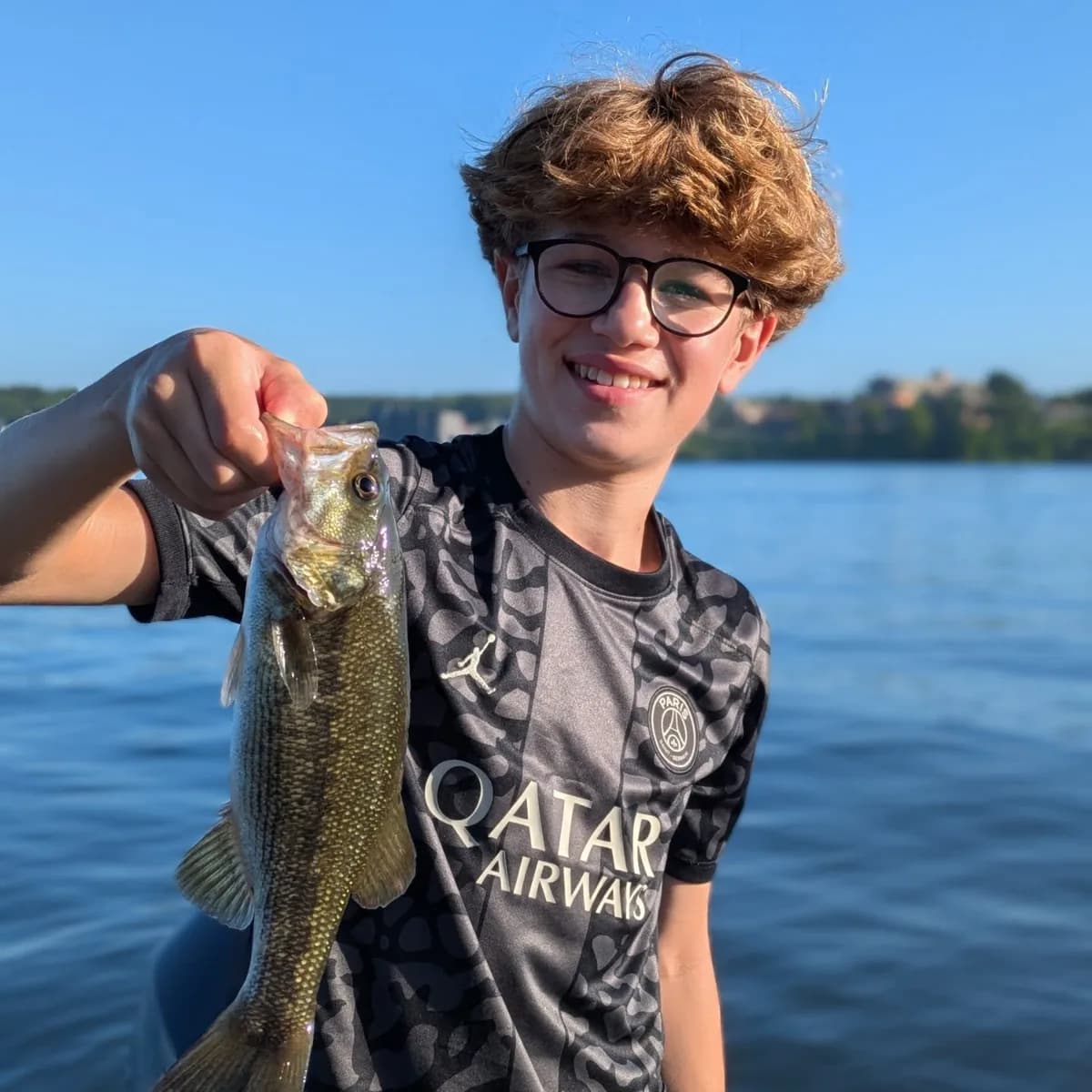 A teenage angler holding out a largemouth bass