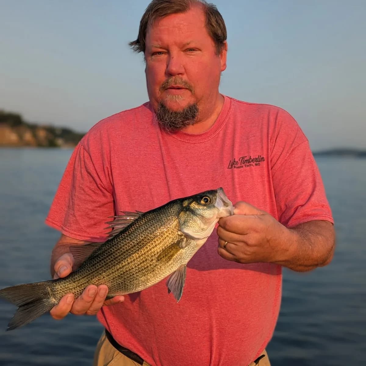 An angler in a red shirt with a largemouth bass