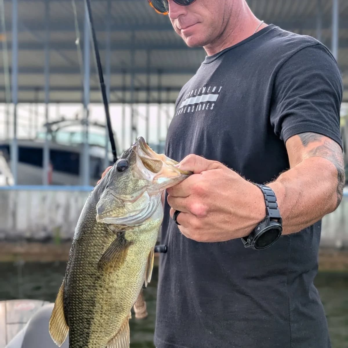 An angler with a largemouth bass beside the boat dock