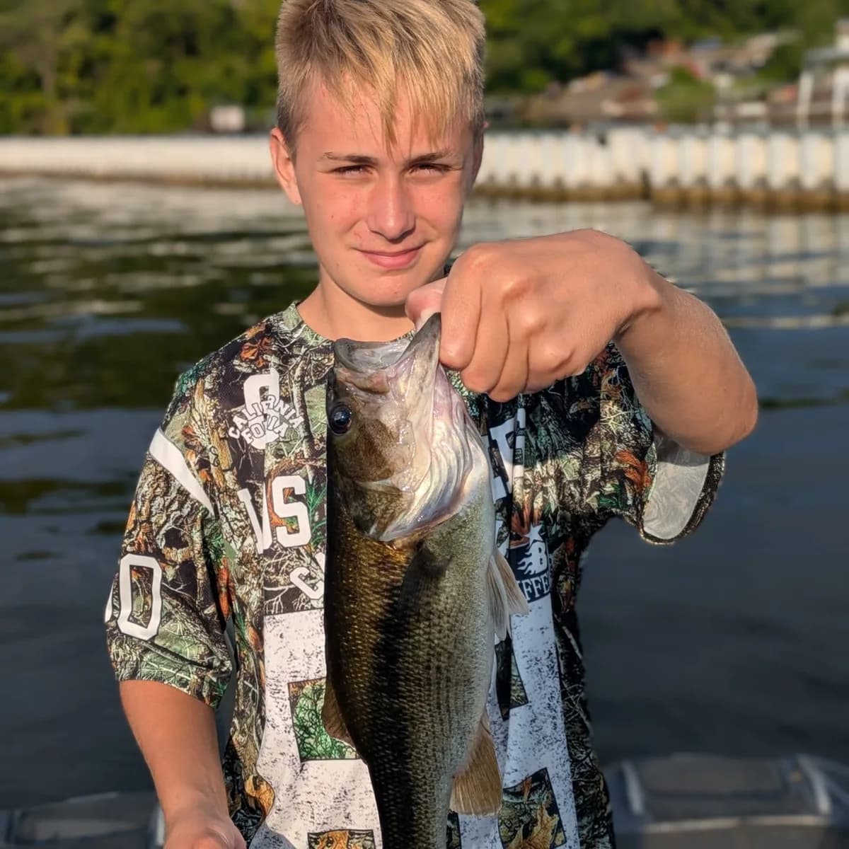 A teenage angler in camo holding a largemouth bass