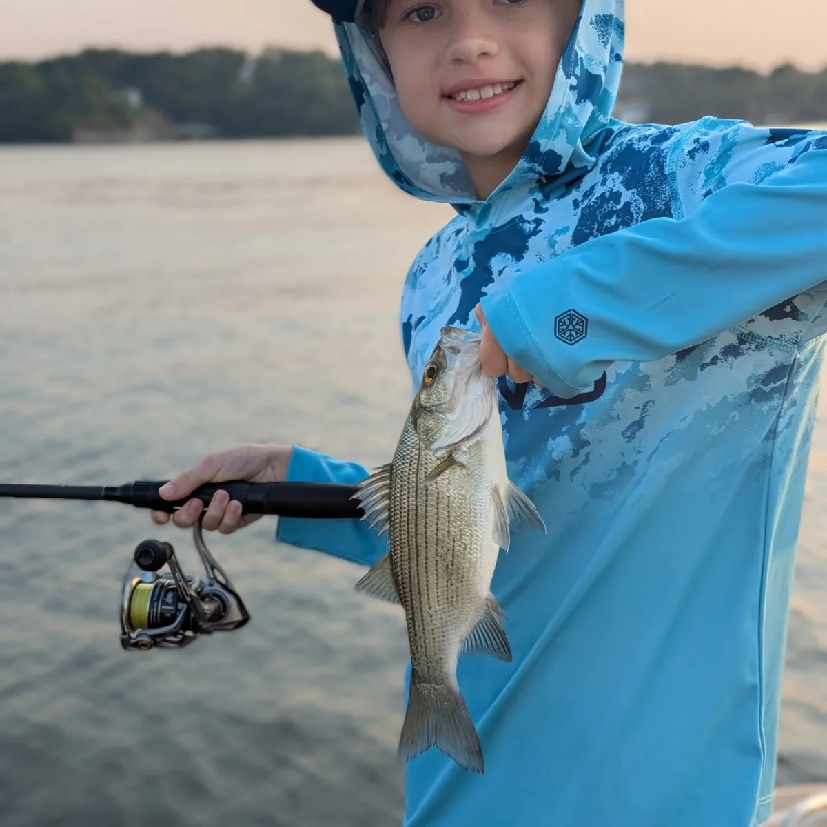 A young angler with a rod in one hand and a largemouth bass in the other