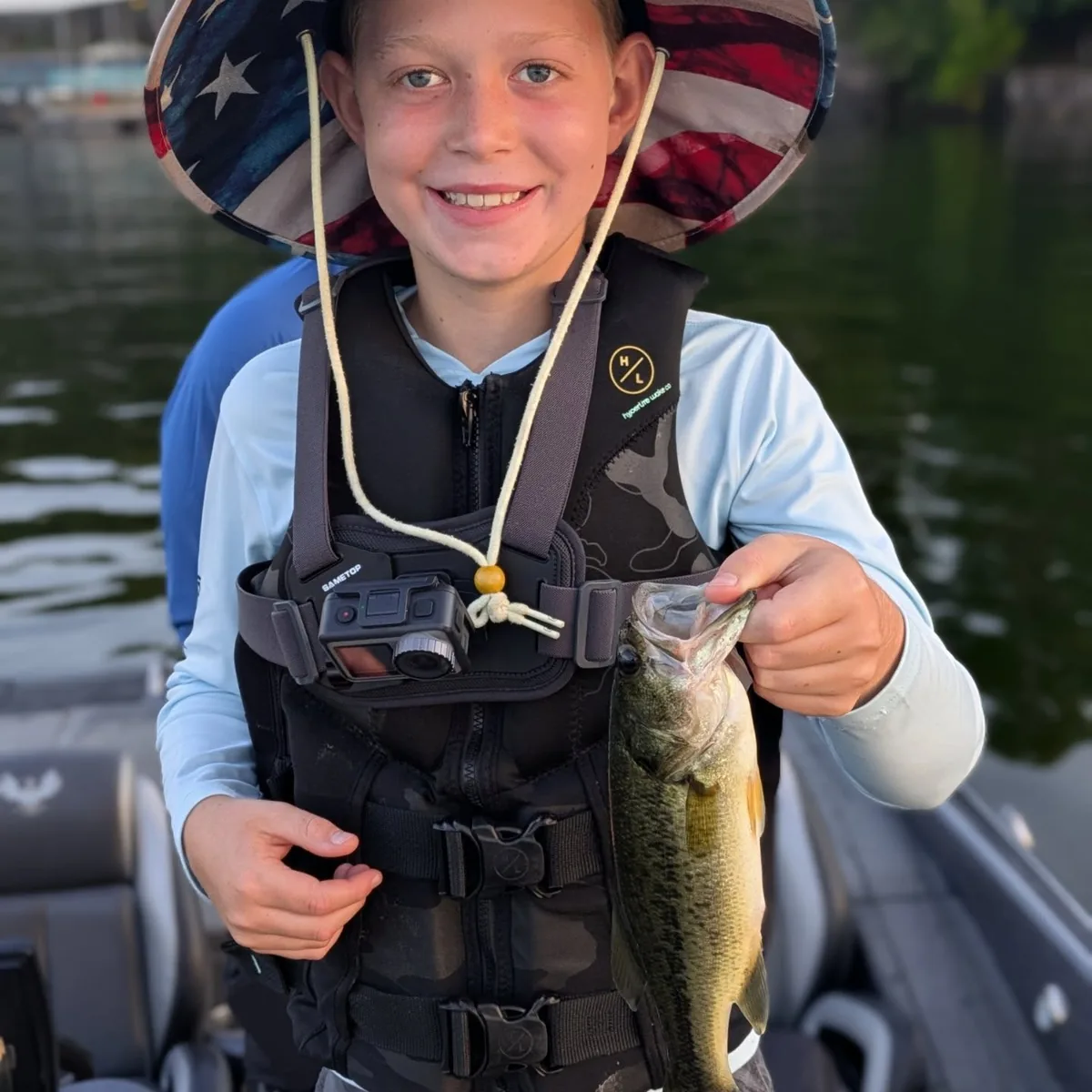 A young angler in a life jacket holding a July largemouth bass