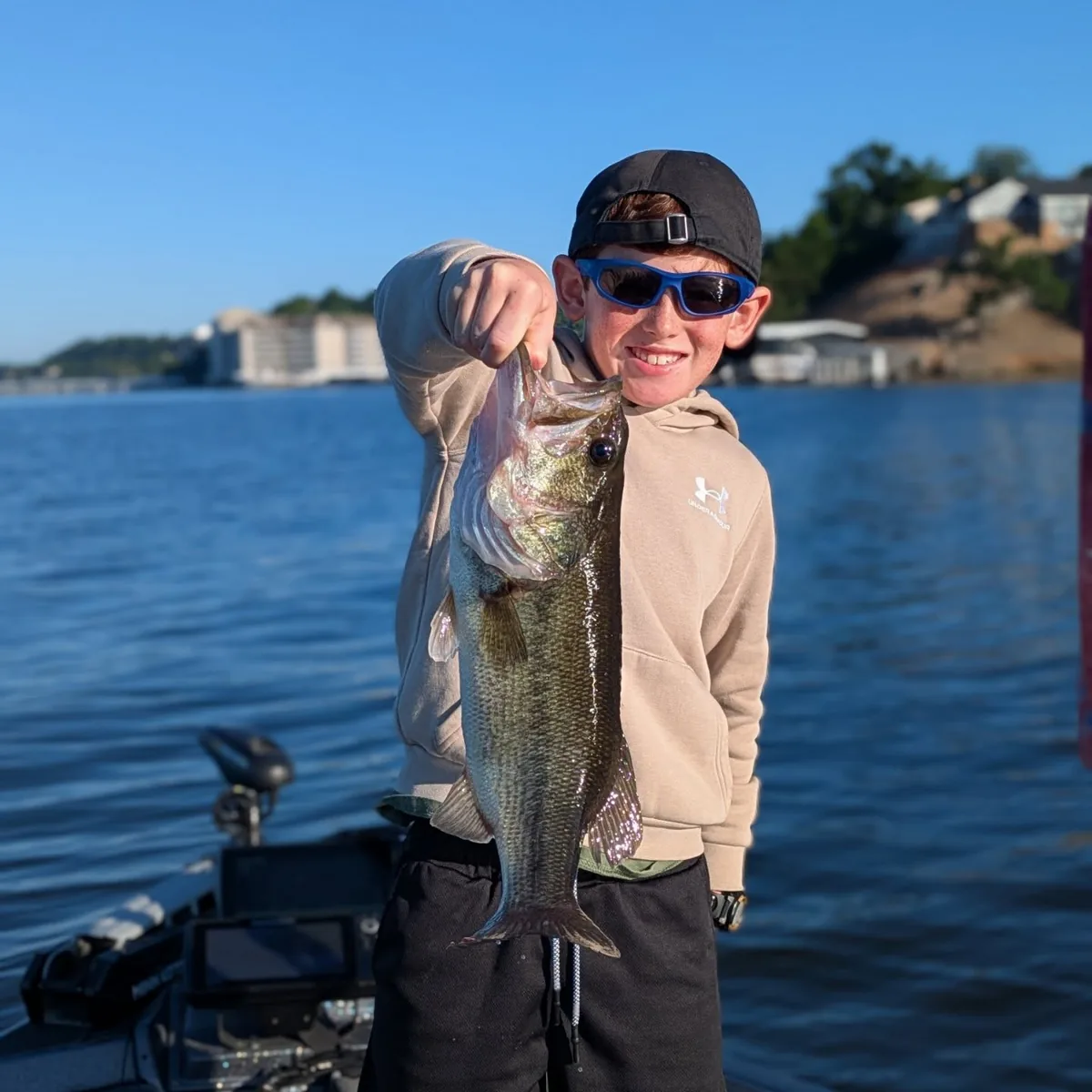 A young angler holding a largemouth bass in front of the shoreline