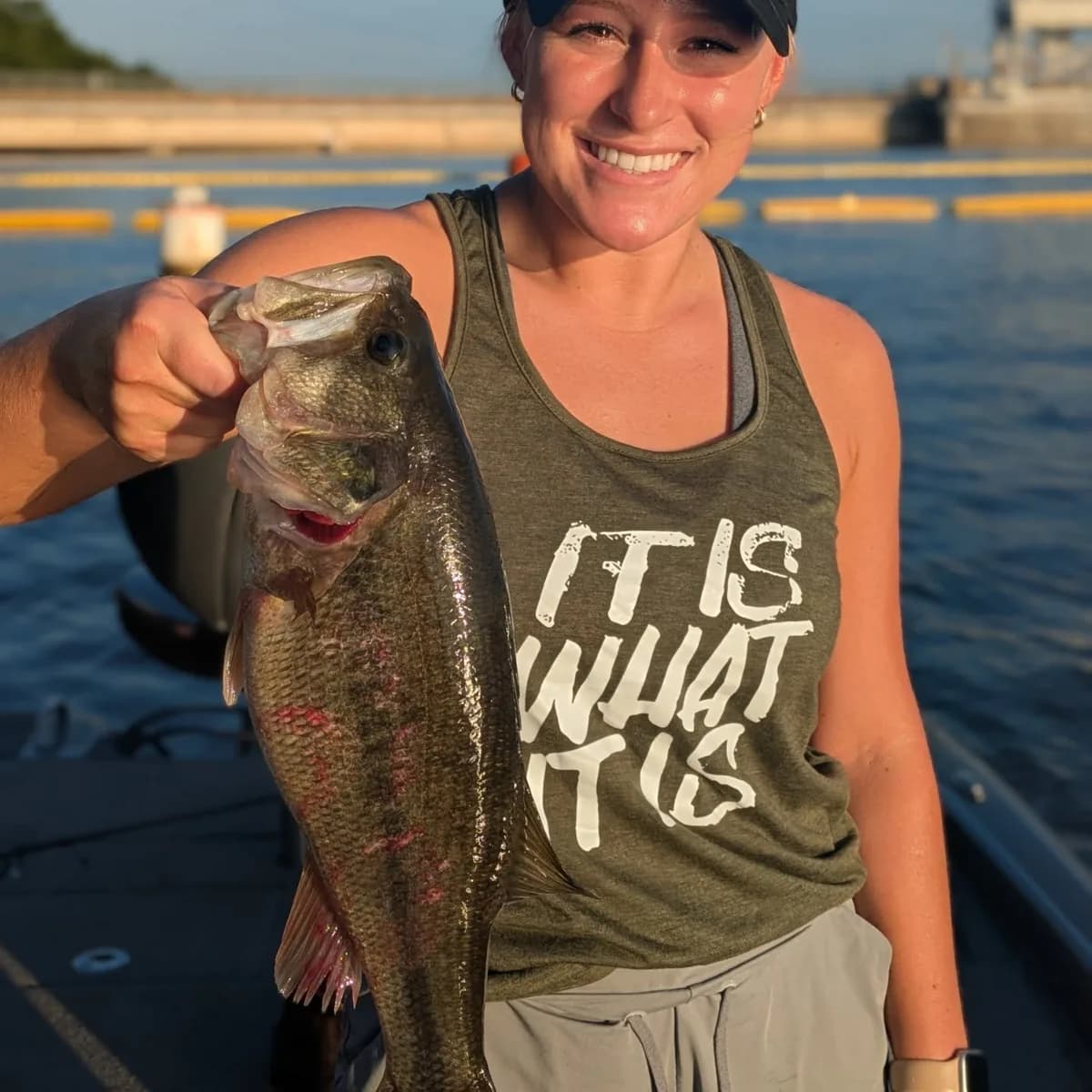 An angler holding a heavy largemouth bass on a warm June morning