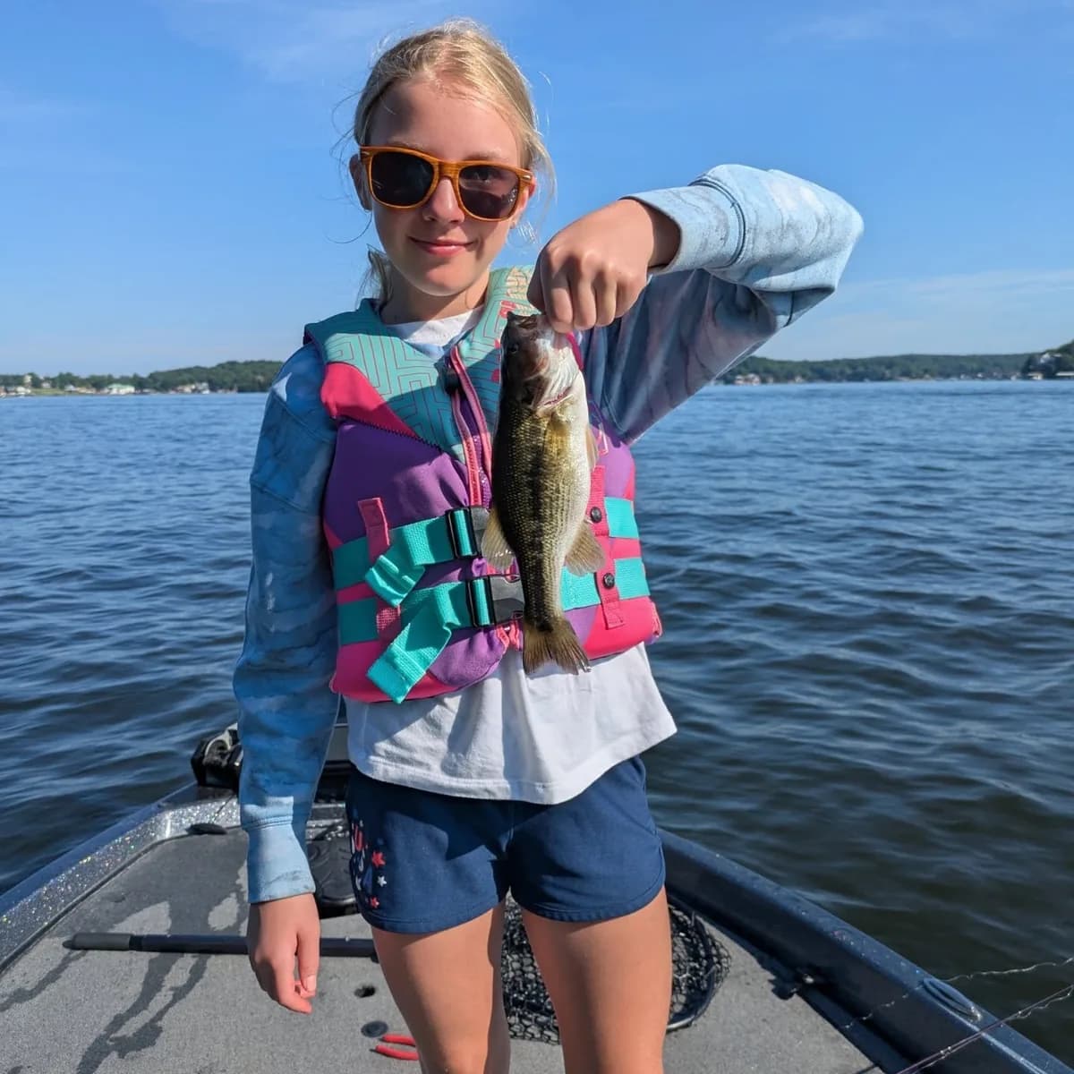 A young angler in a life jacket lifting a largemouth bass