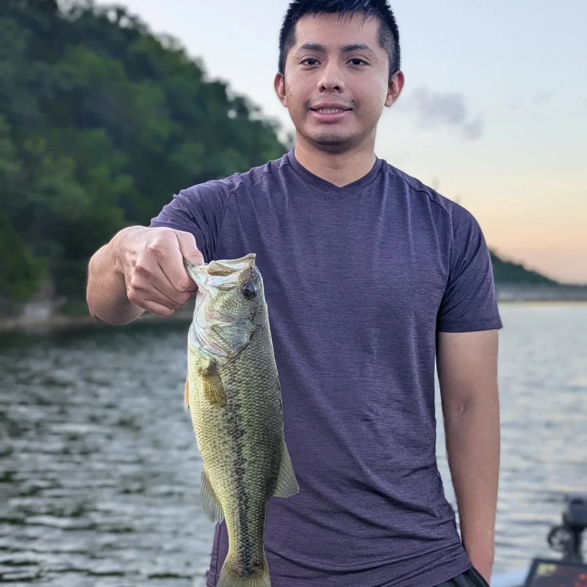 An angler holding a largemouth bass at sunrise