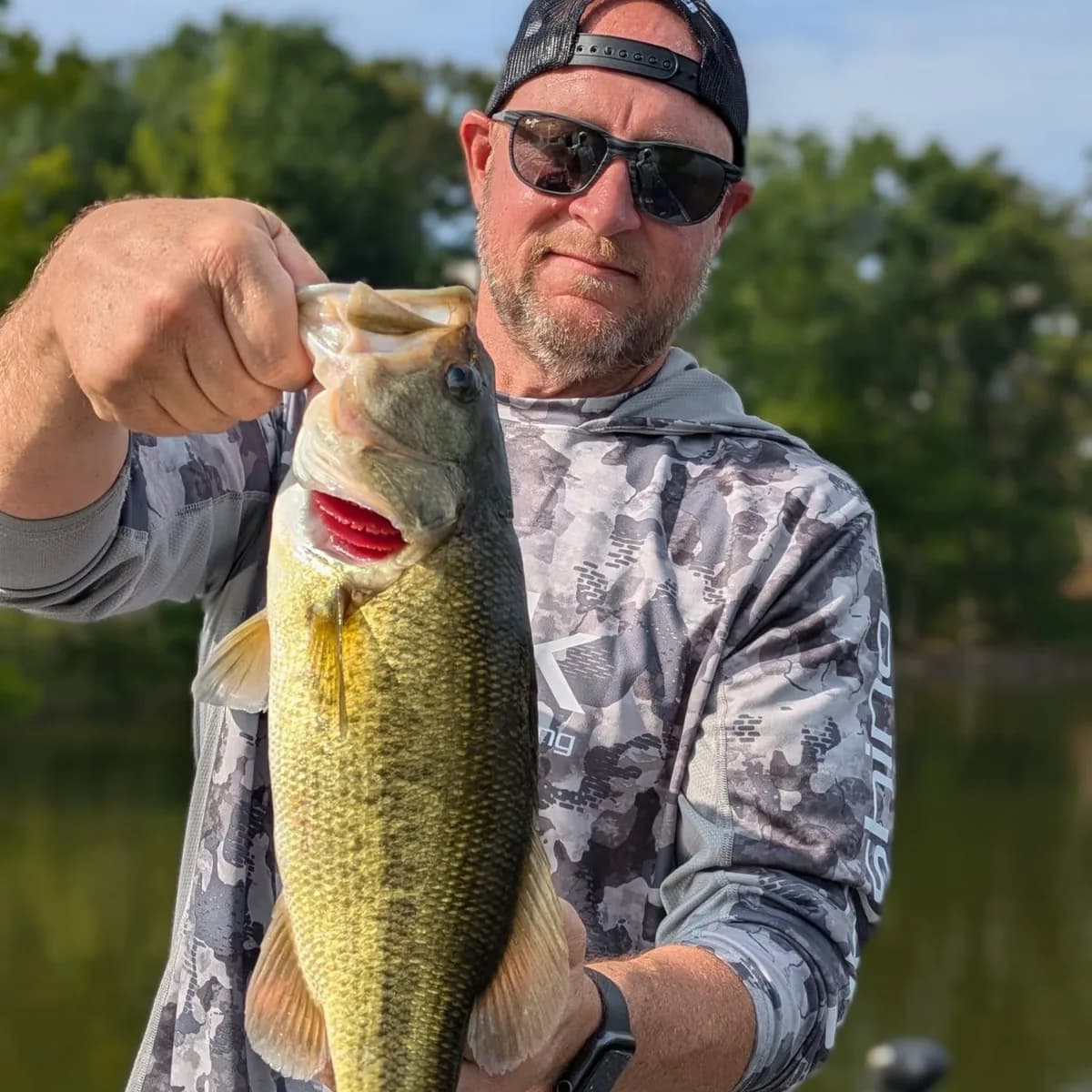 An angler in camo holding a largemouth bass