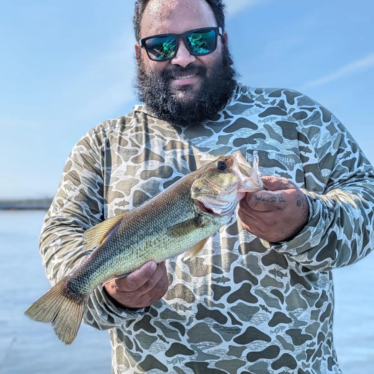 An angler holding a largemouth bass on a bright June day