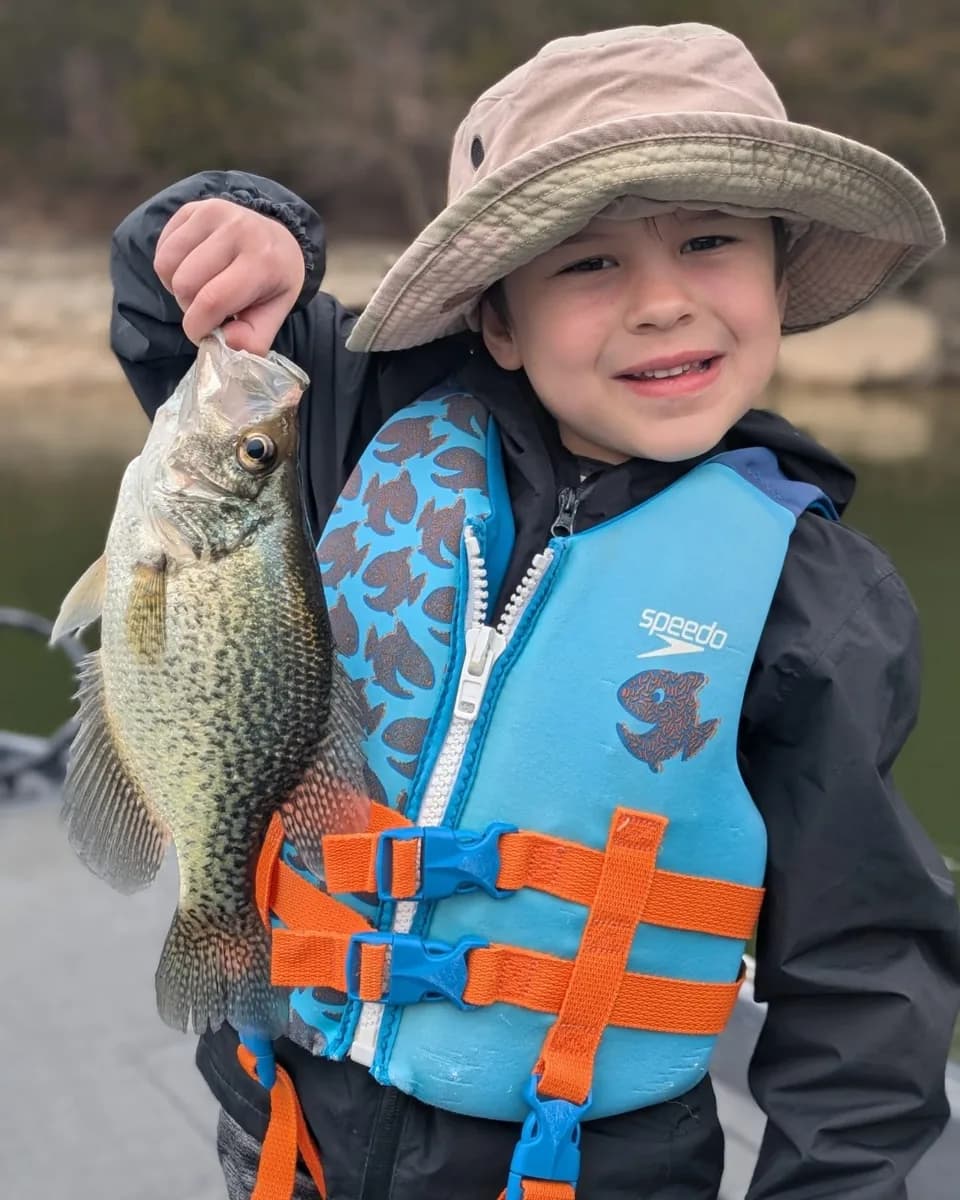A young angler in a life jacket holding a crappie caught in March
