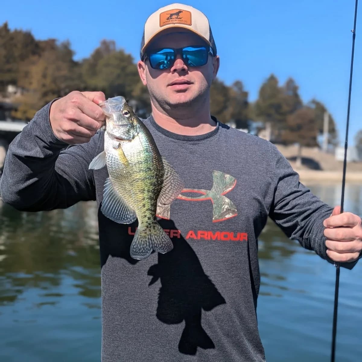 An angler with a crappie and a rod in hand on a bright March day
