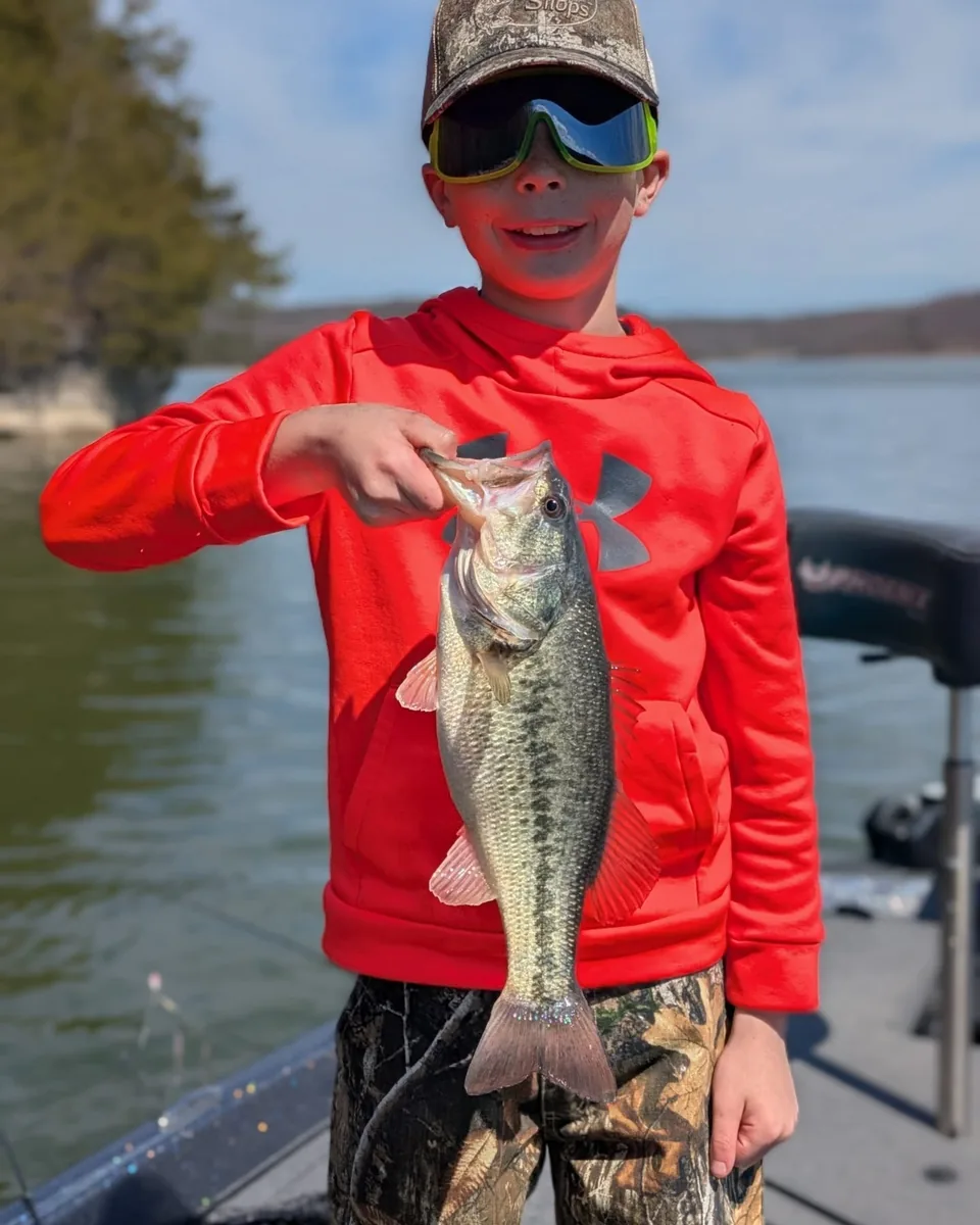 A young angler in a red shirt holding a largemouth bass