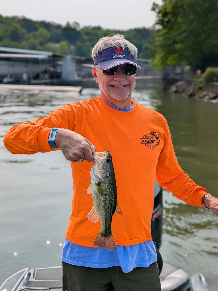 An angler in an orange sun shirt with a May largemouth bass