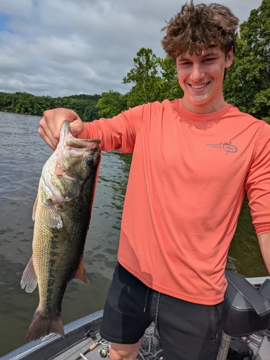 A young angler in a sun shirt holding a heavy largemouth bass