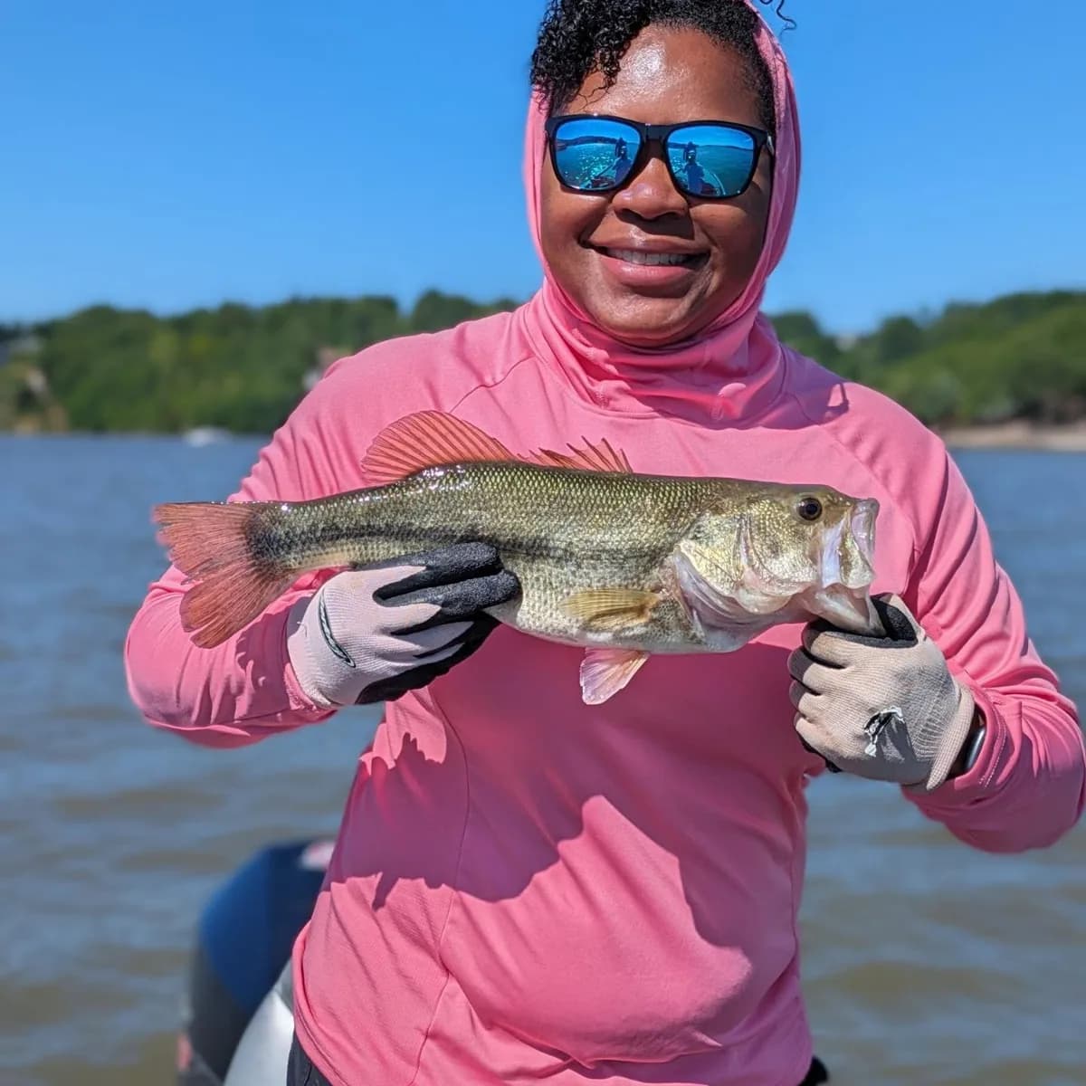 An angler in a sun hoodie holding a May largemouth bass
