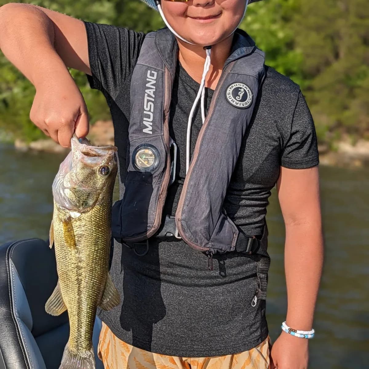 A young angler in a life vest with a largemouth bass