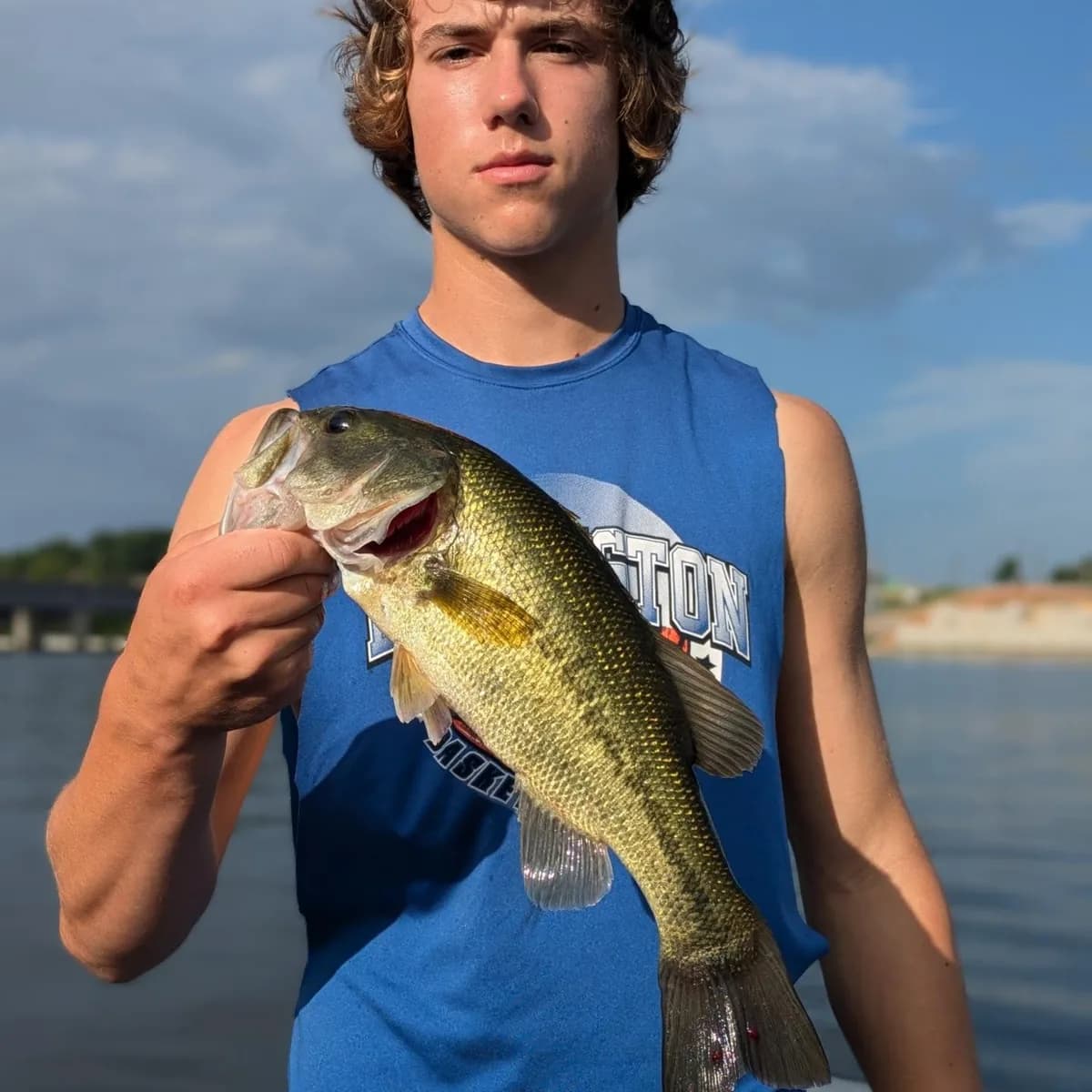 A teenage angler in a sleeveless shirt holding a largemouth bass in September