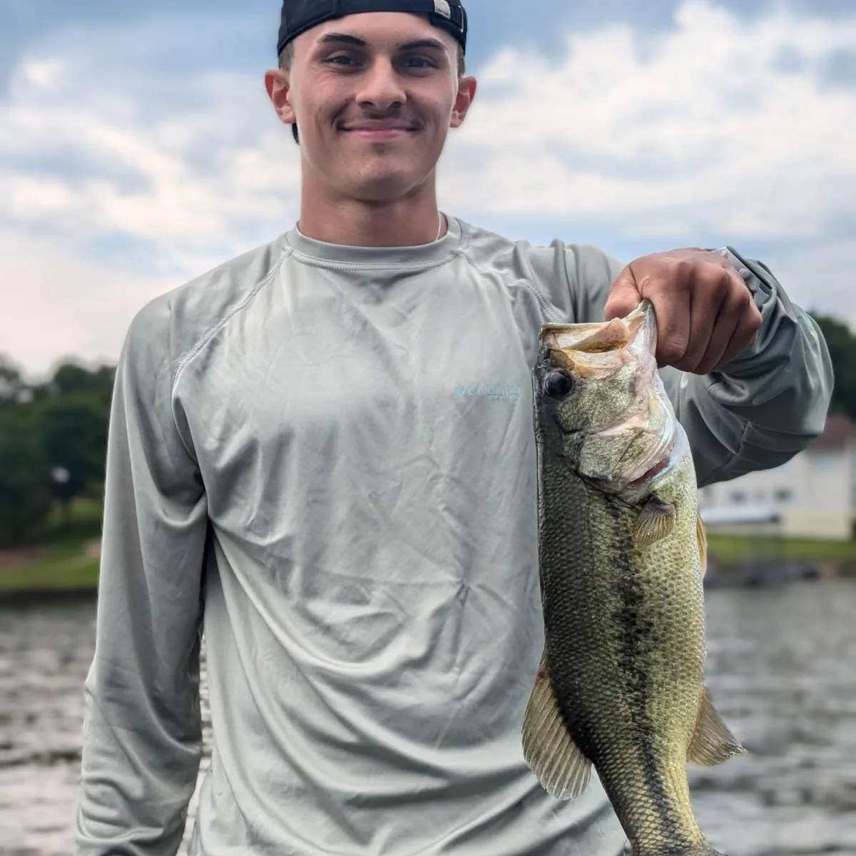 An angler in a sun shirt holding out a largemouth bass on a grey morning