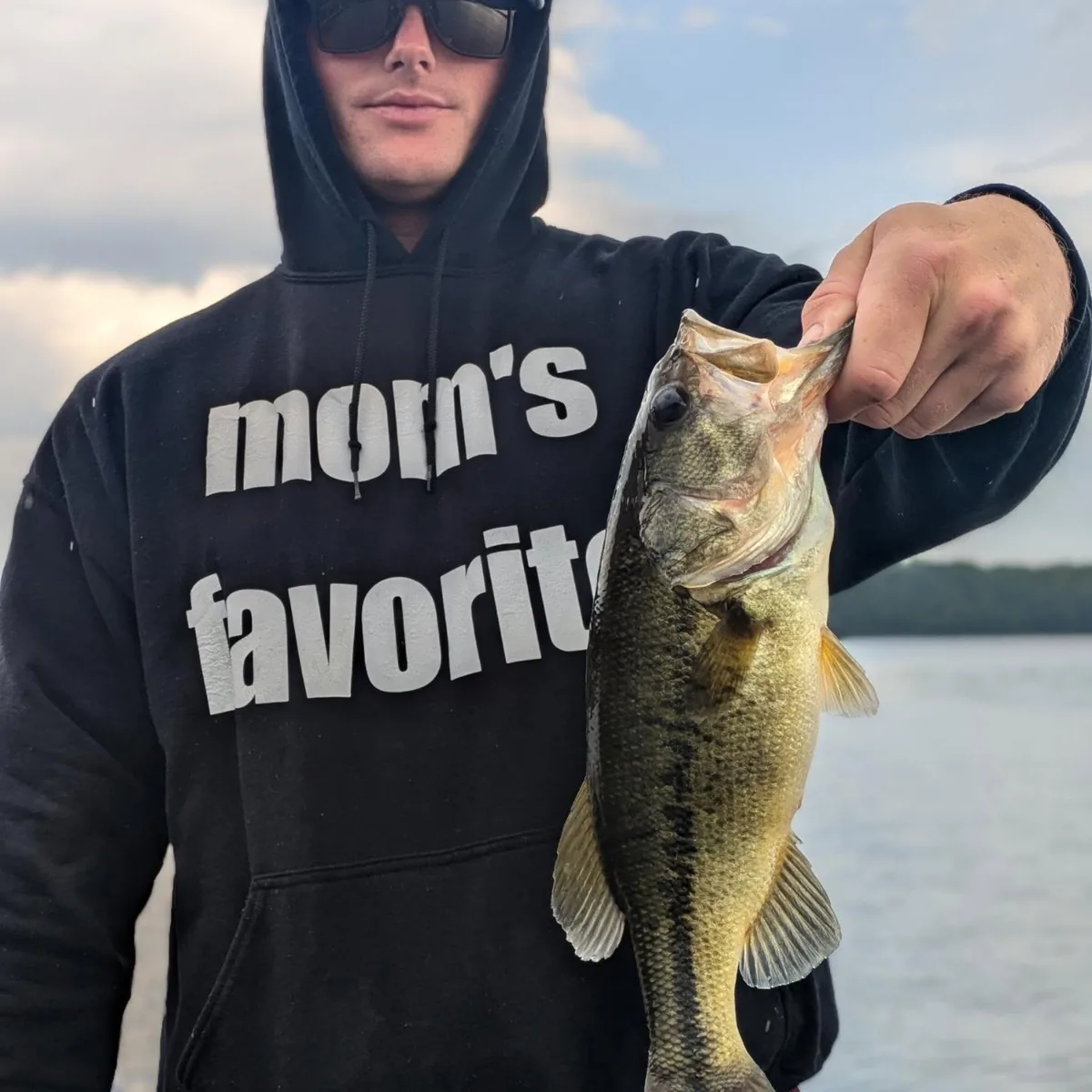 An angler in a hoodie holding a largemouth bass caught on a September trip