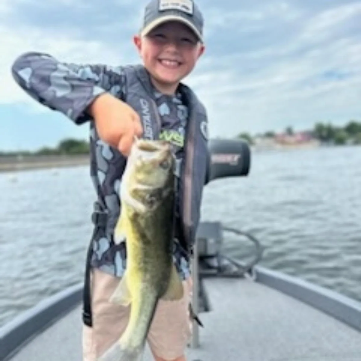 A young angler in a camo shirt holding up a largemouth bass