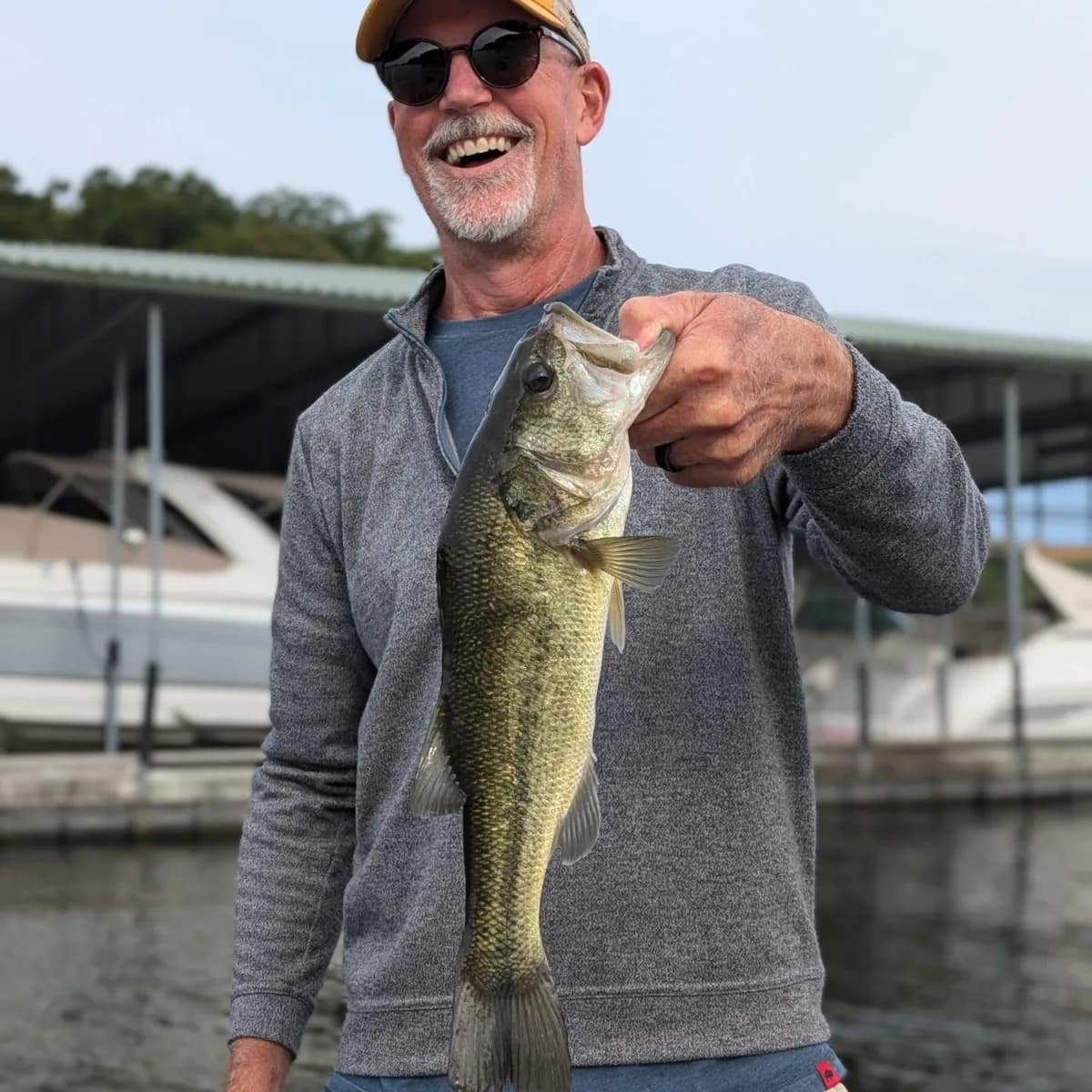 An angler holding a largemouth bass in front of a covered boat dock