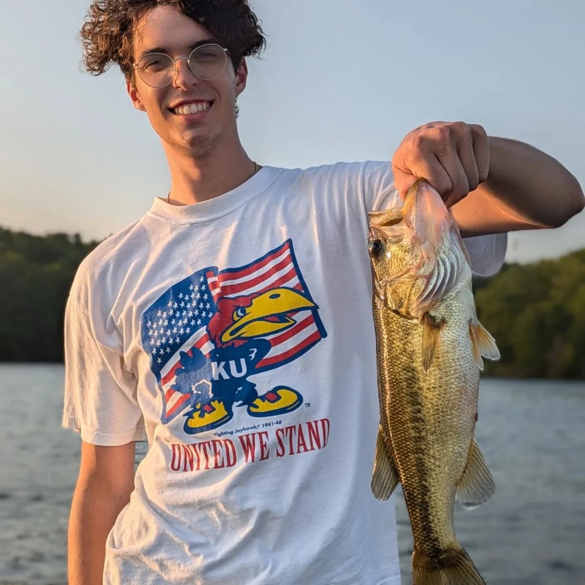 A teenage angler holding a largemouth bass at arm's length
