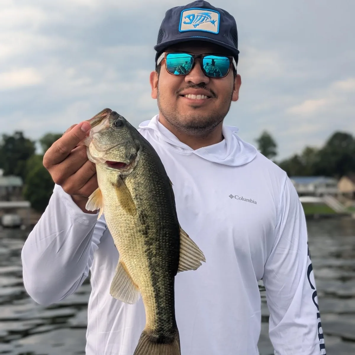 An angler in a sun shirt with a largemouth bass on an overcast day