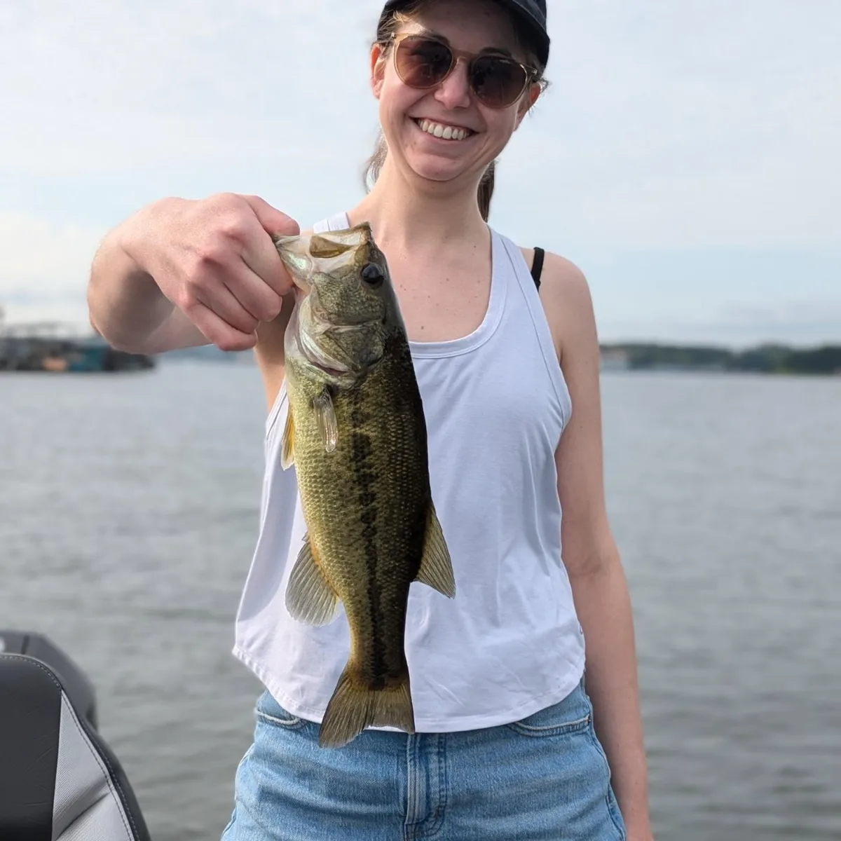 An angler in a tank top holding out a largemouth bass on a hot September day